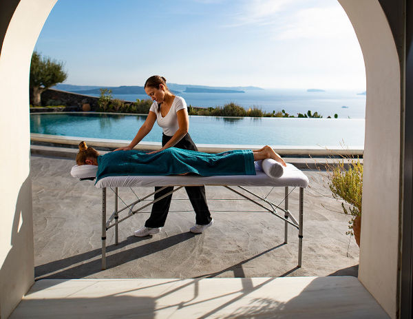 A massage therapist performing the Zen Ritual for Couples, using aromatherapy oils and providing a facial massage to a relaxed woman on a villa's massage table.